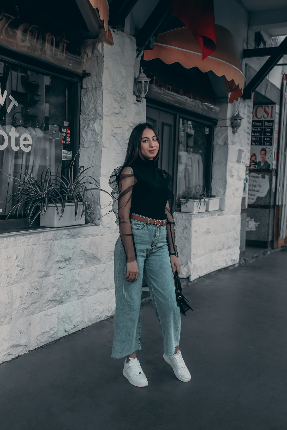 woman in black shirt and blue denim jeans standing beside white concrete wall during daytime